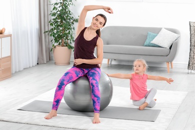 Sportive woman doing fitness exercises with daughter at home