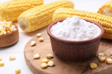 Photo of Bowl with corn starch and kernels on white table, closeup