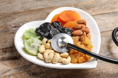 Photo of Heart shaped plate with dried fruits, nuts and stethoscope on wooden background