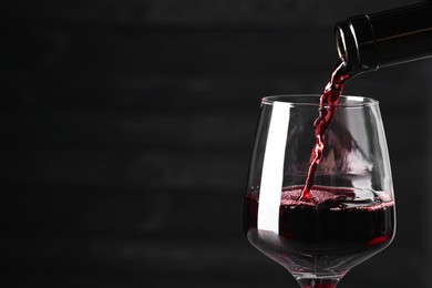 Pouring red wine into glass against dark background, closeup. Space for text