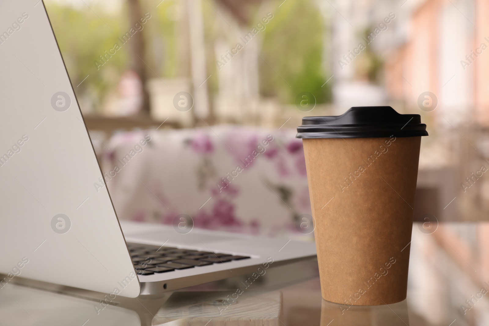 Photo of Cup of aromatic morning coffee and laptop on table in cafe