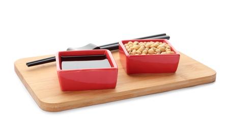 Photo of Wooden board with dishes of soy sauce and beans on white background