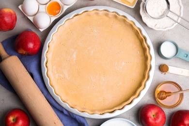 Photo of Raw dough and ingredients for traditional English apple pie on light grey table, flat lay