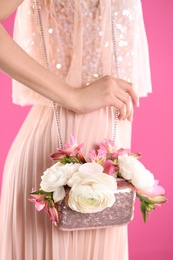 Woman holding elegant handbag with spring flowers on pink background, closeup