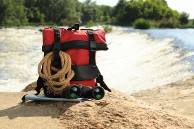 Backpack and camping equipment on stone near river. Space for text