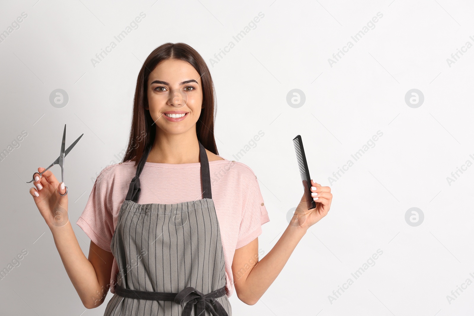 Photo of Young hairstylist holding professional scissors and comb on light background