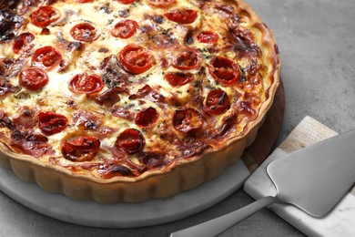 Photo of Delicious homemade prosciutto quiche and spatula on gray table, closeup