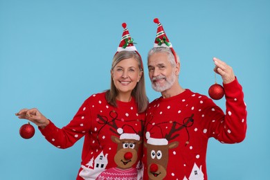 Photo of Senior couple in Christmas sweaters holding festive baubles on light blue background