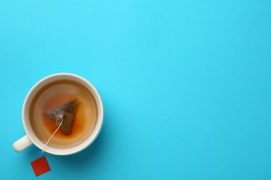 Photo of Tea bag in cup of hot water on light blue background, top view. Space for text