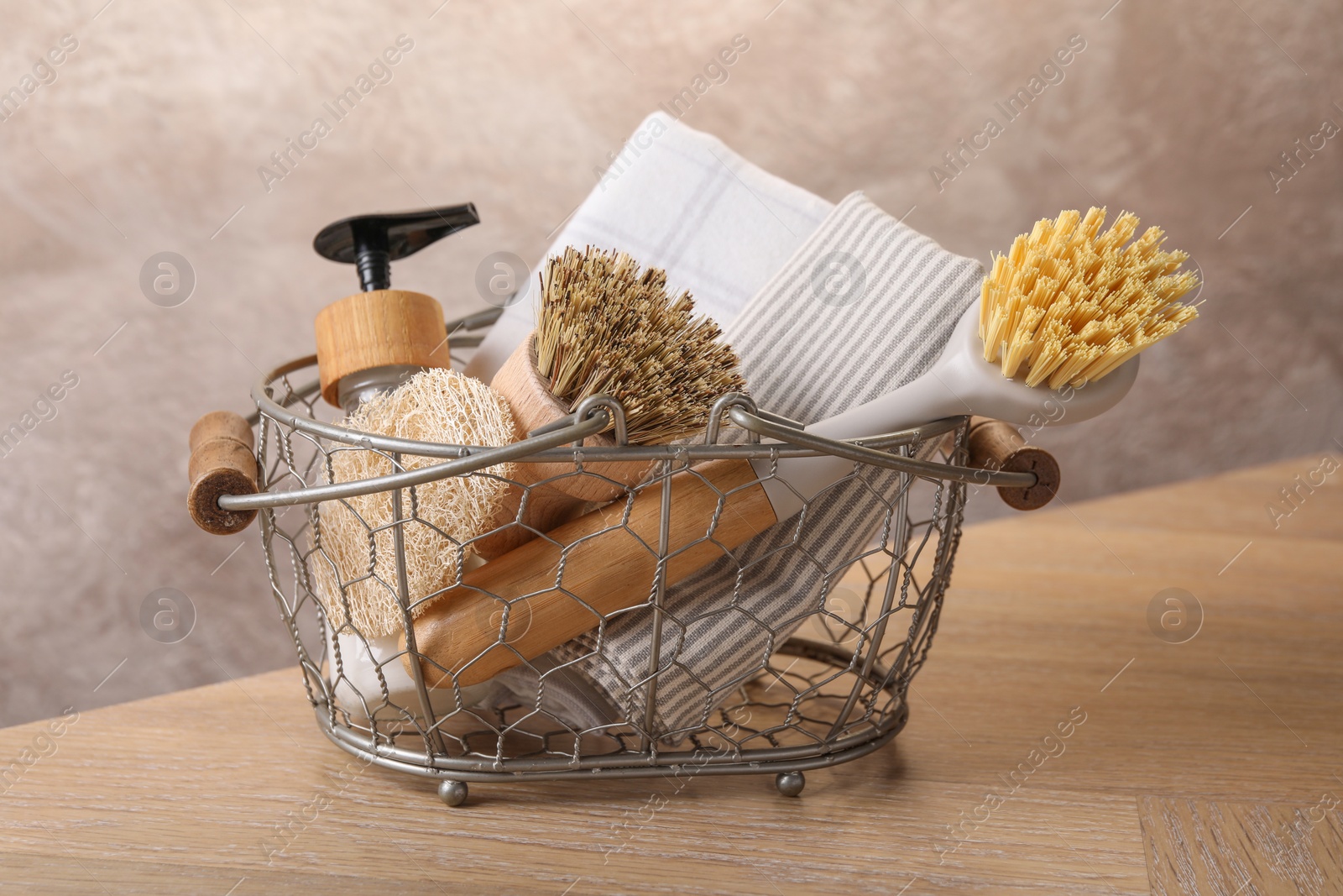 Photo of Metal basket with brushes and cleaning tools on wooden table