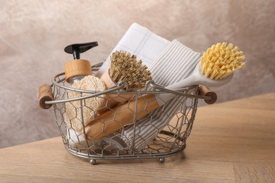 Photo of Metal basket with brushes and cleaning tools on wooden table