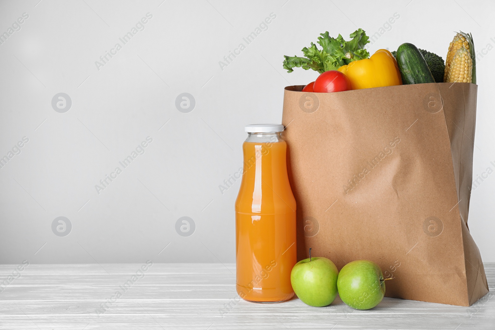 Photo of Paper bag with fresh vegetables and other products on white wooden table against light background, space for text