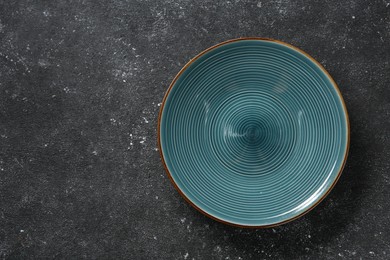 Photo of One ceramic plate on black textured table, top view. Space for text