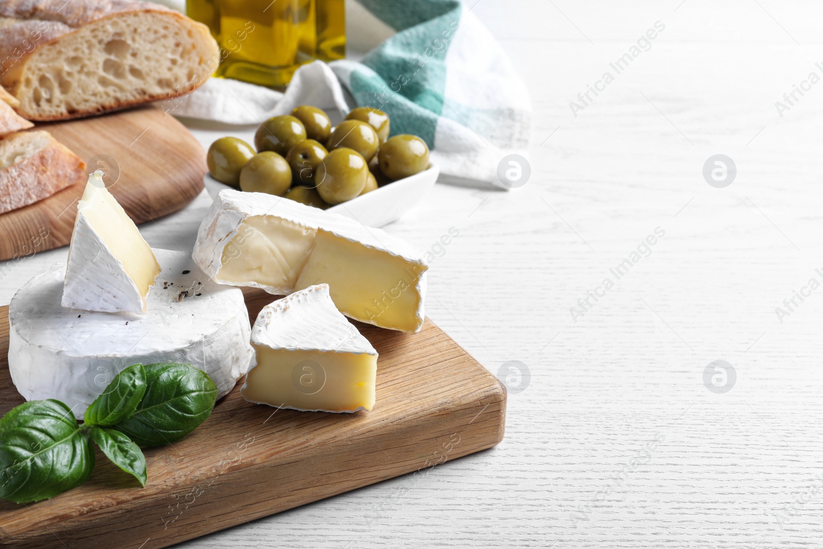 Photo of Tasty brie cheese with basil on white wooden table, space for text