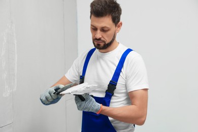 Professional worker with putty knives and plaster near wall indoors