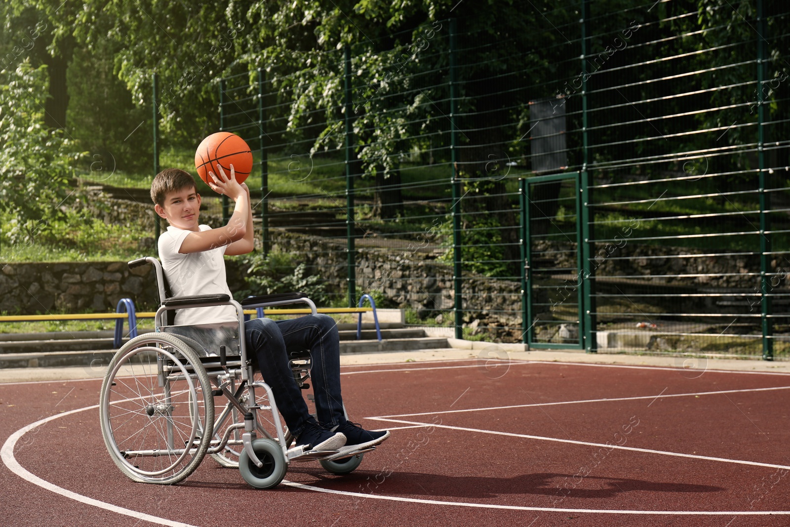 Photo of Disabled teenage boy in wheelchair playing basketball  on outdoor court