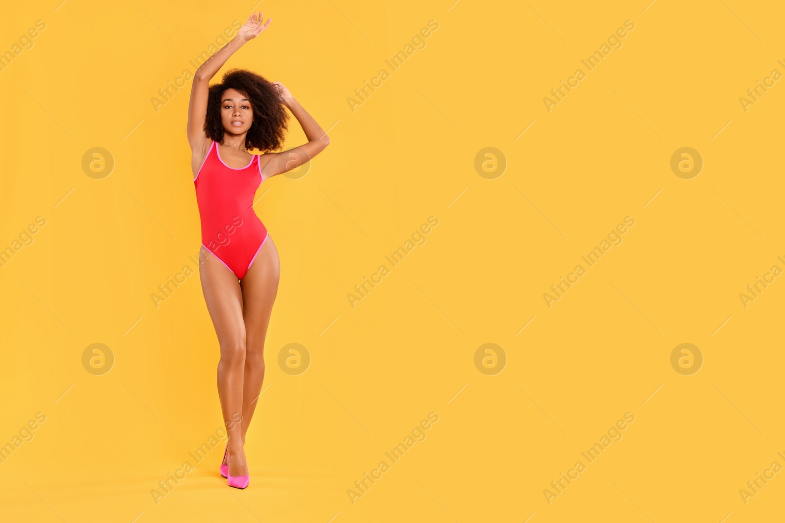 Photo of Beautiful woman in bright one-piece summer swimsuit and stylish high heel shoes on yellow background, space for text