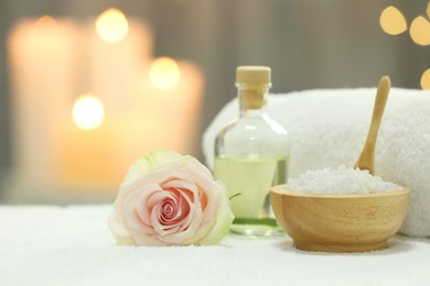 Photo of Beautiful spa composition with essential oil, sea salt and rose on white towel against blurred background. Space for text