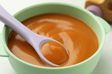 Photo of Bowl and spoon with tasty pureed baby food on table, closeup