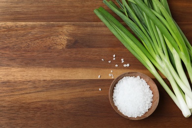 Photo of Fresh green onions and bowl of salt on wooden background, top view. Space for text