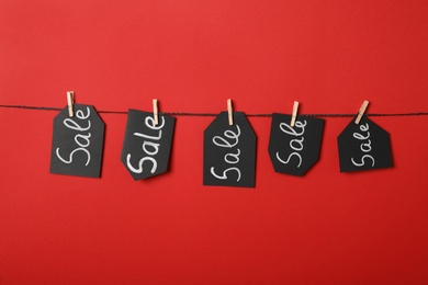 Photo of Tags with word Sale hanging on rope against red background. Black Friday concept