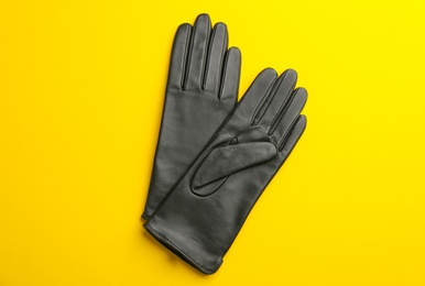 Photo of Pair of stylish leather gloves on yellow background, flat lay