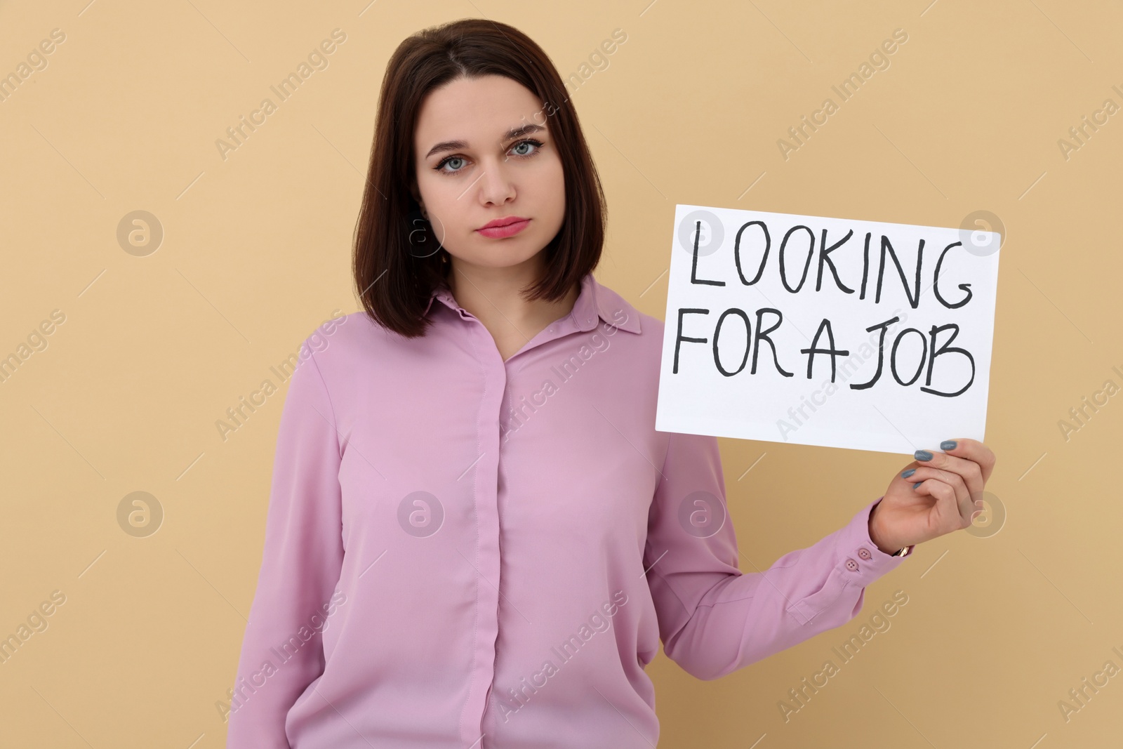 Photo of Young unemployed woman holding sign with phrase Looking For A Job on beige background