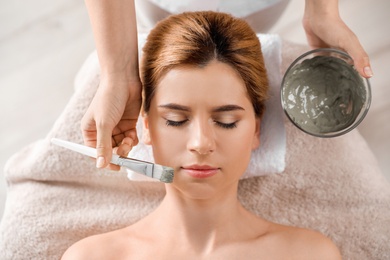 Photo of Cosmetologist applying mask onto woman's face in spa salon, top view