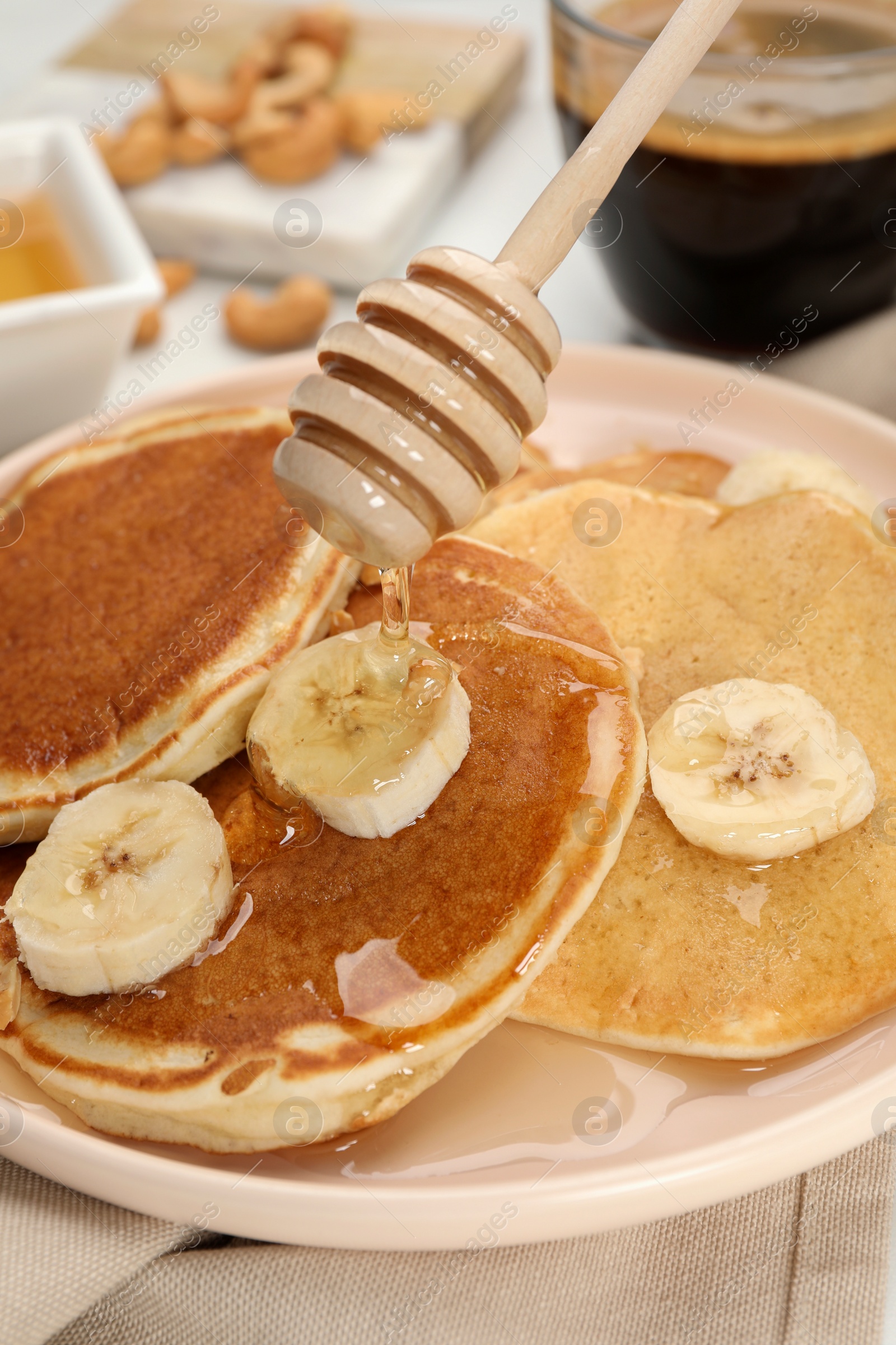 Photo of Pouring honey onto pancakes with banana on table, closeup