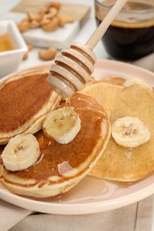 Photo of Pouring honey onto pancakes with banana on table, closeup
