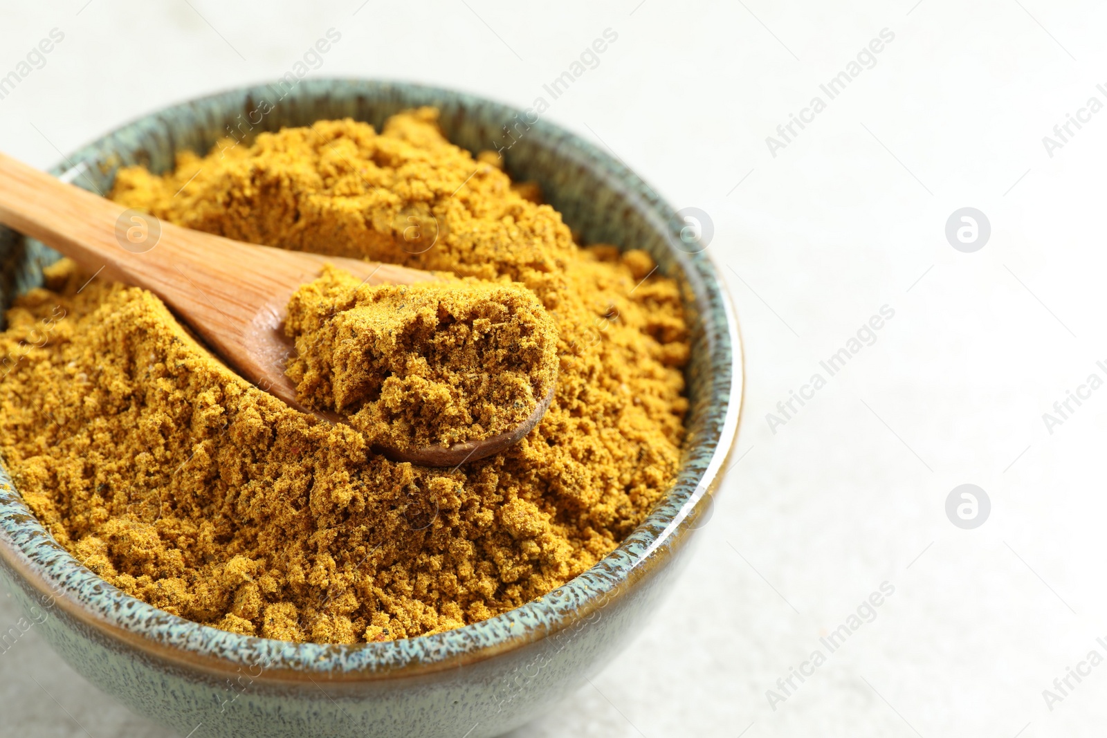 Photo of Dry curry powder in bowl and spoon on light table, closeup