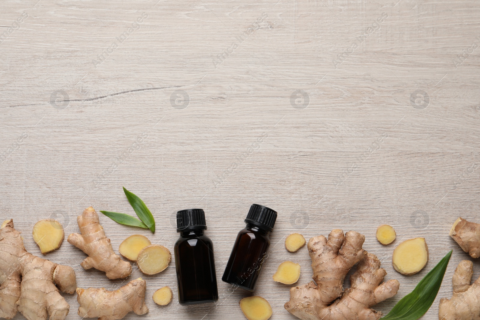 Photo of Glass bottles of essential oil and ginger root on white wooden table, flat lay. Space for text