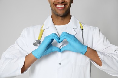 Photo of Doctor or medical assistant (male nurse) in uniform making heart with hands on light grey background, closeup