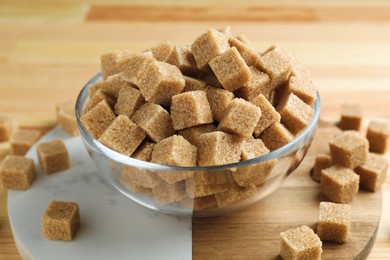 Photo of Brown sugar cubes in bowl on wooden table, closeup