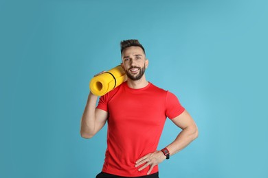 Handsome man with yoga mat on turquoise background