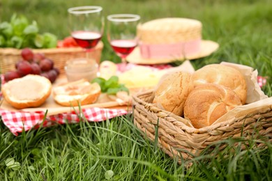 Photo of Picnic blanket with wine and snacks outdoors, focus on buns in wicker basket