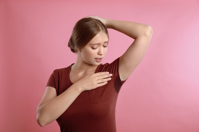 Photo of Young woman with sweat stain on her clothes against pink background. Using deodorant