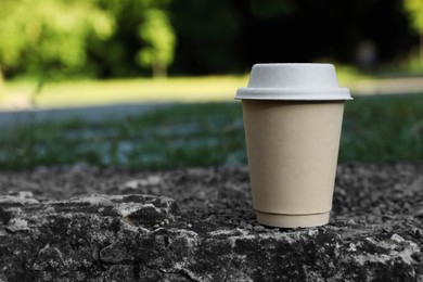 Photo of Cardboard takeaway coffee cup with lid on stone surface outdoors, space for text