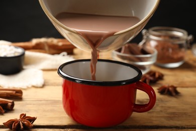 Photo of Pouring tasty hot chocolate into cup at wooden table, closeup