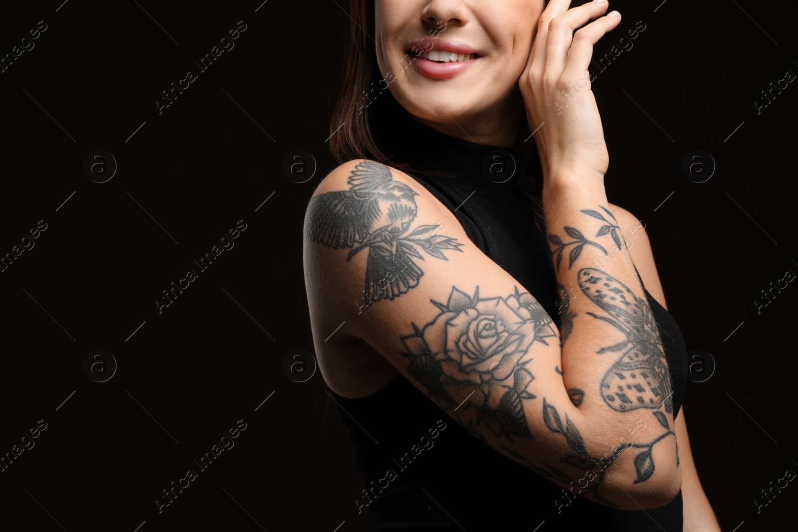 Photo of Beautiful woman with tattoos on arm against black background, closeup. Space for text