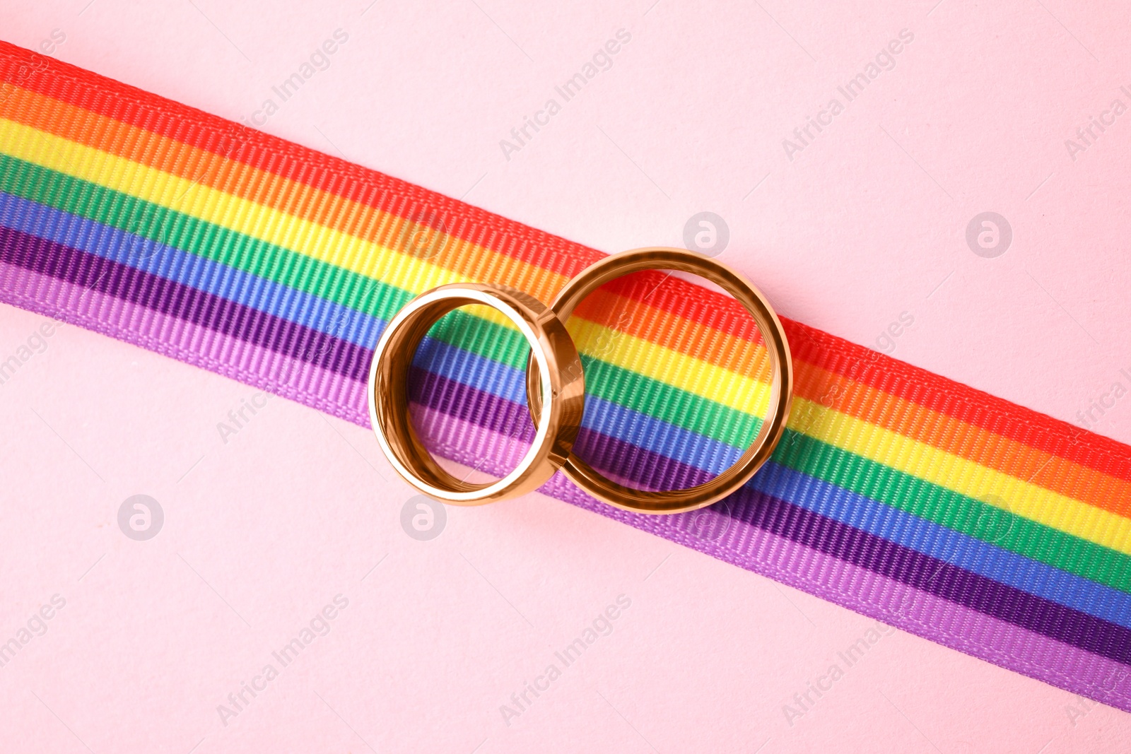 Photo of Wedding rings and rainbow ribbon on color background, top view. Gay symbol