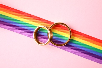 Photo of Wedding rings and rainbow ribbon on color background, top view. Gay symbol