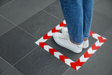 Photo of Woman standing on taped floor marking for social distance, closeup. Coronavirus pandemic