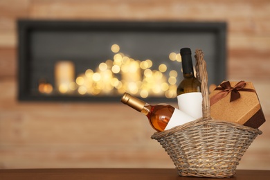 Photo of Wicker basket with bottles of wine and gift box on table in room. Space for text