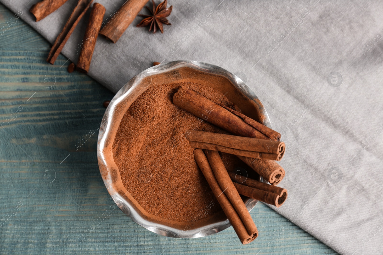 Photo of Bowl with aromatic cinnamon powder and sticks on wooden background