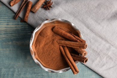 Bowl with aromatic cinnamon powder and sticks on wooden background