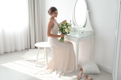 Young bride in wedding dress with beautiful bouquet near mirror indoors