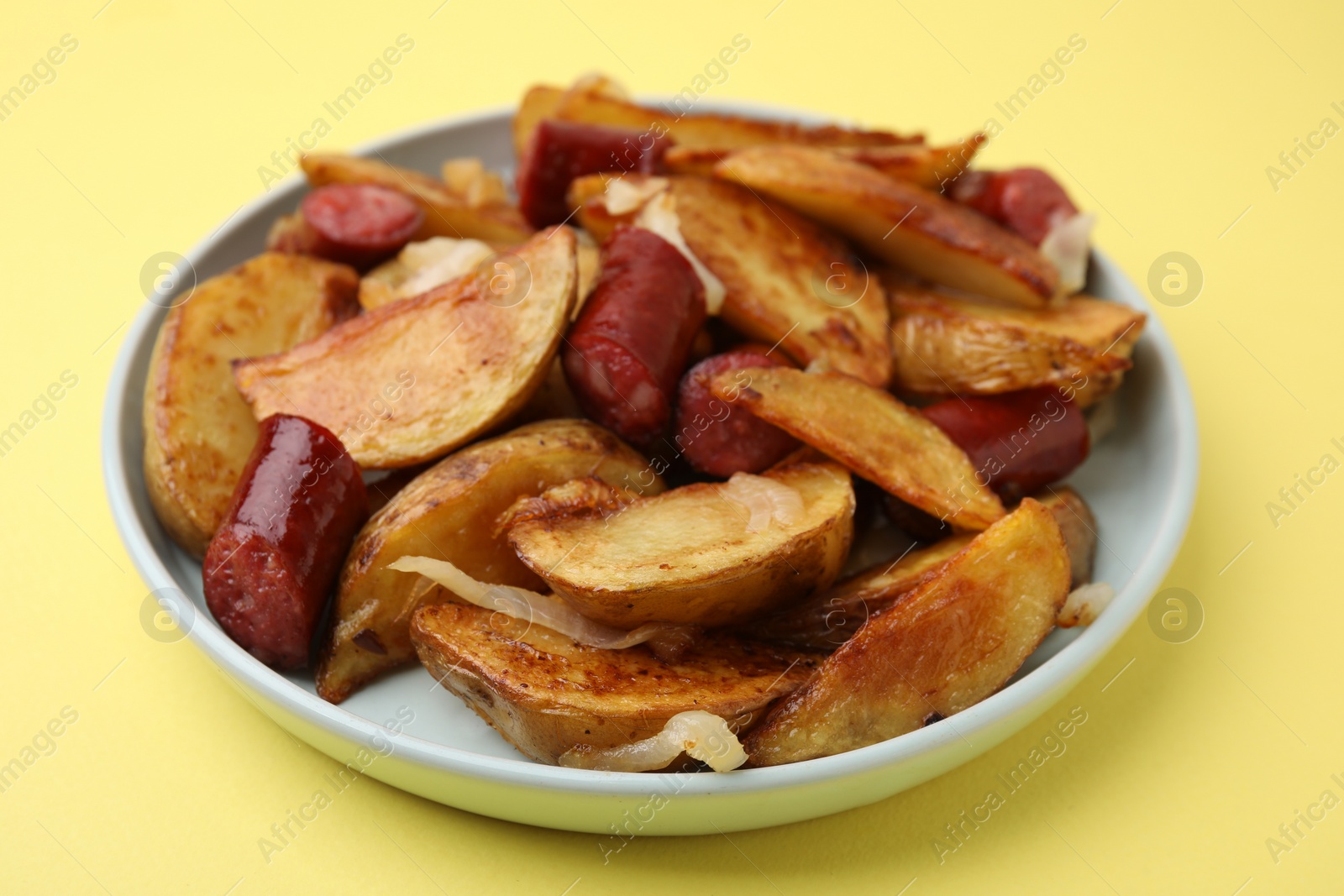 Photo of Delicious baked potato with thin dry smoked sausages and onion on yellow table, closeup