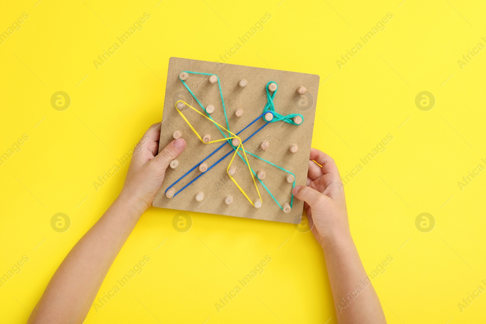Photo of Motor skills development. Boy with geoboard and rubber bands at yellow table, top view