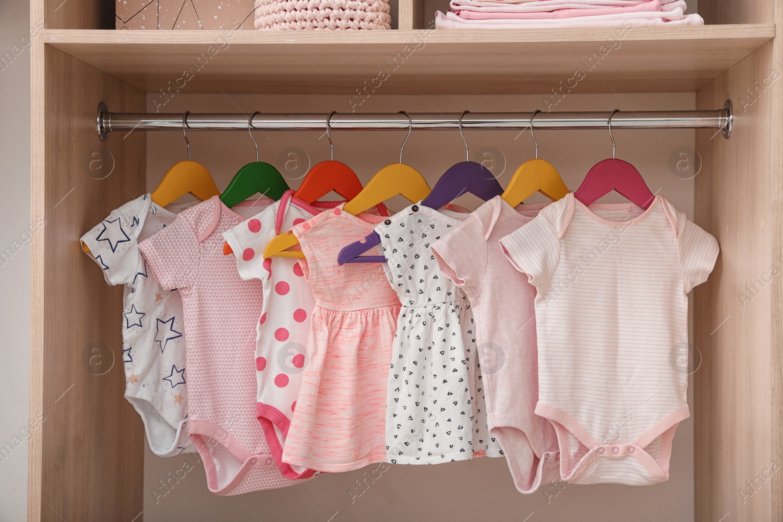 Photo of Hangers with baby clothes on rack in wardrobe